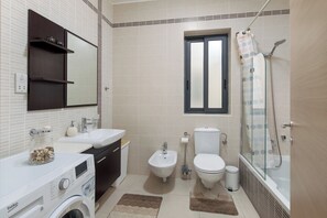 A modern bathroom with a washing machine, bidet, toilet, and glass-enclosed shower. - Luxury 3 BR Apartment - heart of Sliema (Sliema)