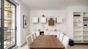 Ein moderner Essbereich mit einem Holztisch und weißen Stühlen, einer weißen Wand mit gerahmten Kunstwerken und Dekoration sowie einem Bücherregal mit Büchern und Deko-Objekten.