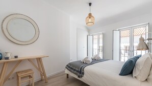 Ein Schlafzimmer mit Bett, Nachttisch, Stuhl und einem großen Spiegel.
