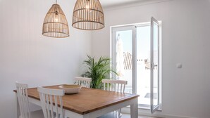 Ein Essbereich mit Holztisch, weißen Stühlen, einer Topfpflanze und Blick durch eine Glastür.
