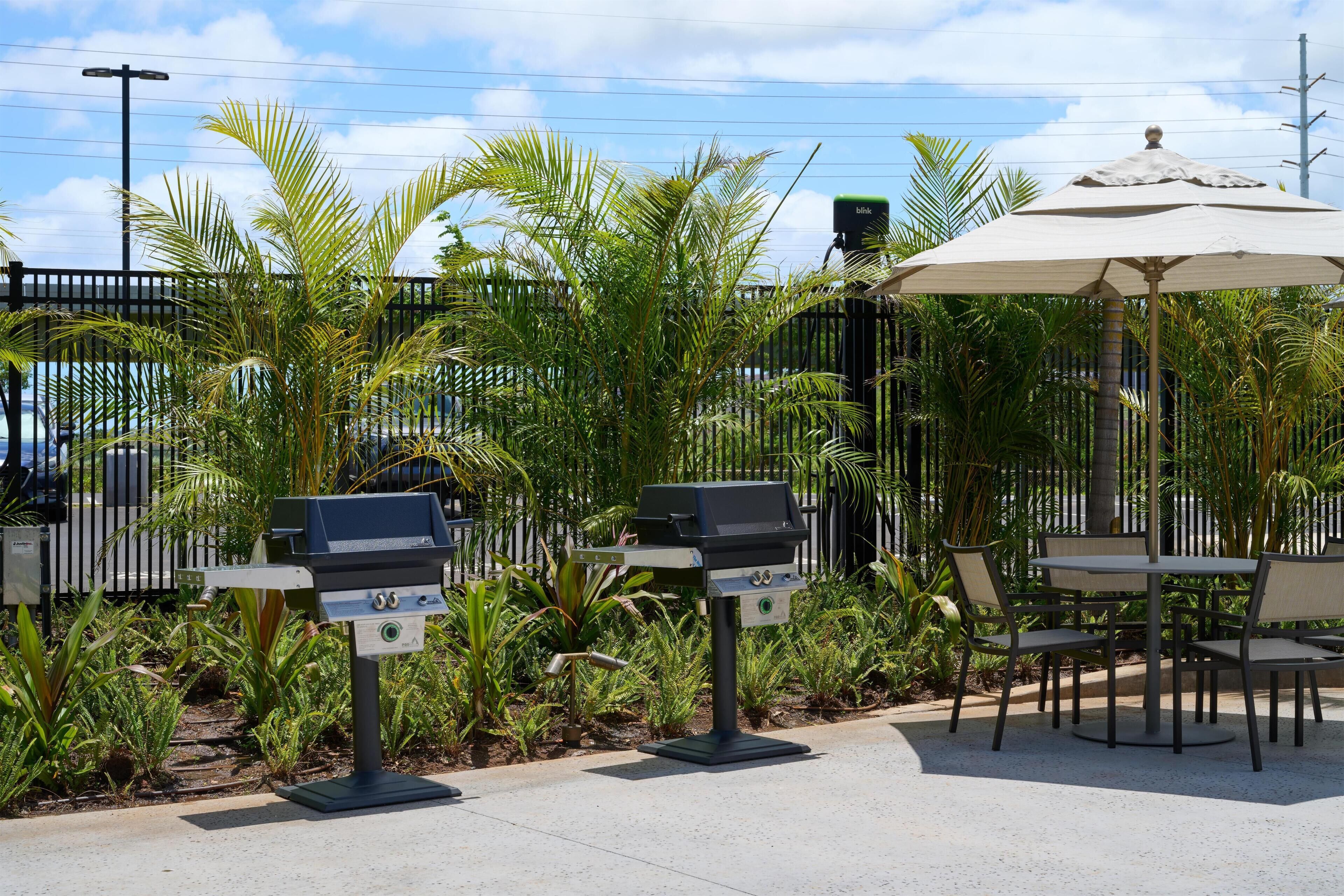 Eine Terrasse mit Außengrills, einem Tisch und Stühlen sowie einem großen Sonnenschirm.