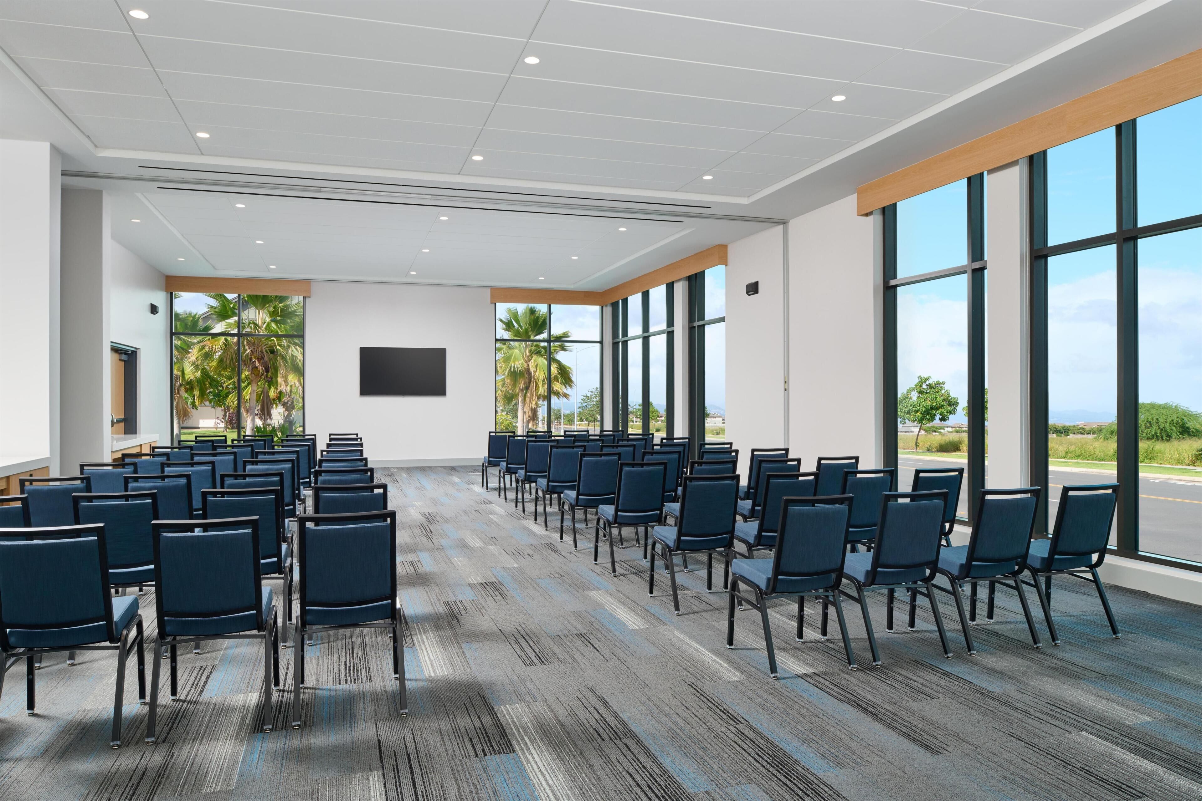 A conference room with rows of chairs, large windows, and a flat-screen TV on the wall.