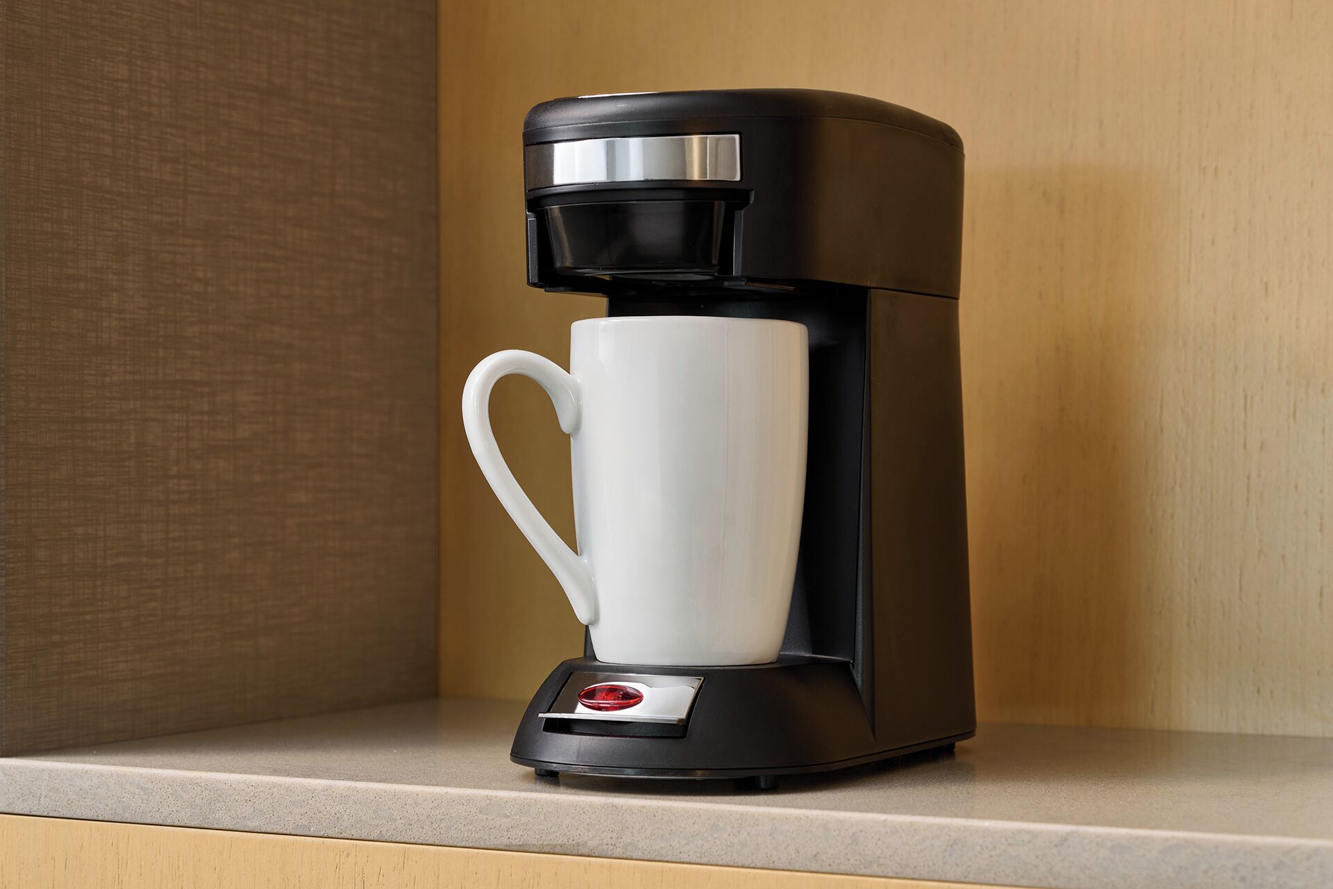 A black coffee maker with a white mug on a countertop.