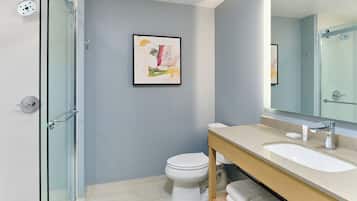 Un baño moderno con cabina de ducha de vidrio, inodoro blanco, tocador beige con espejo y un cuadro abstracto enmarcado en la pared.