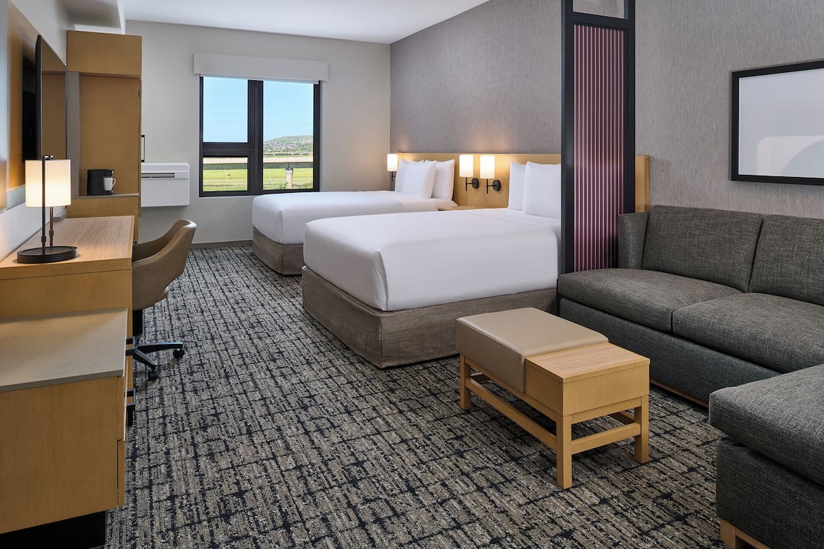 A hotel room with two beds, a sofa, a desk, and a small table.