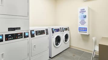 A laundry facility with multiple washing machines, a soap dispenser, and a chair.