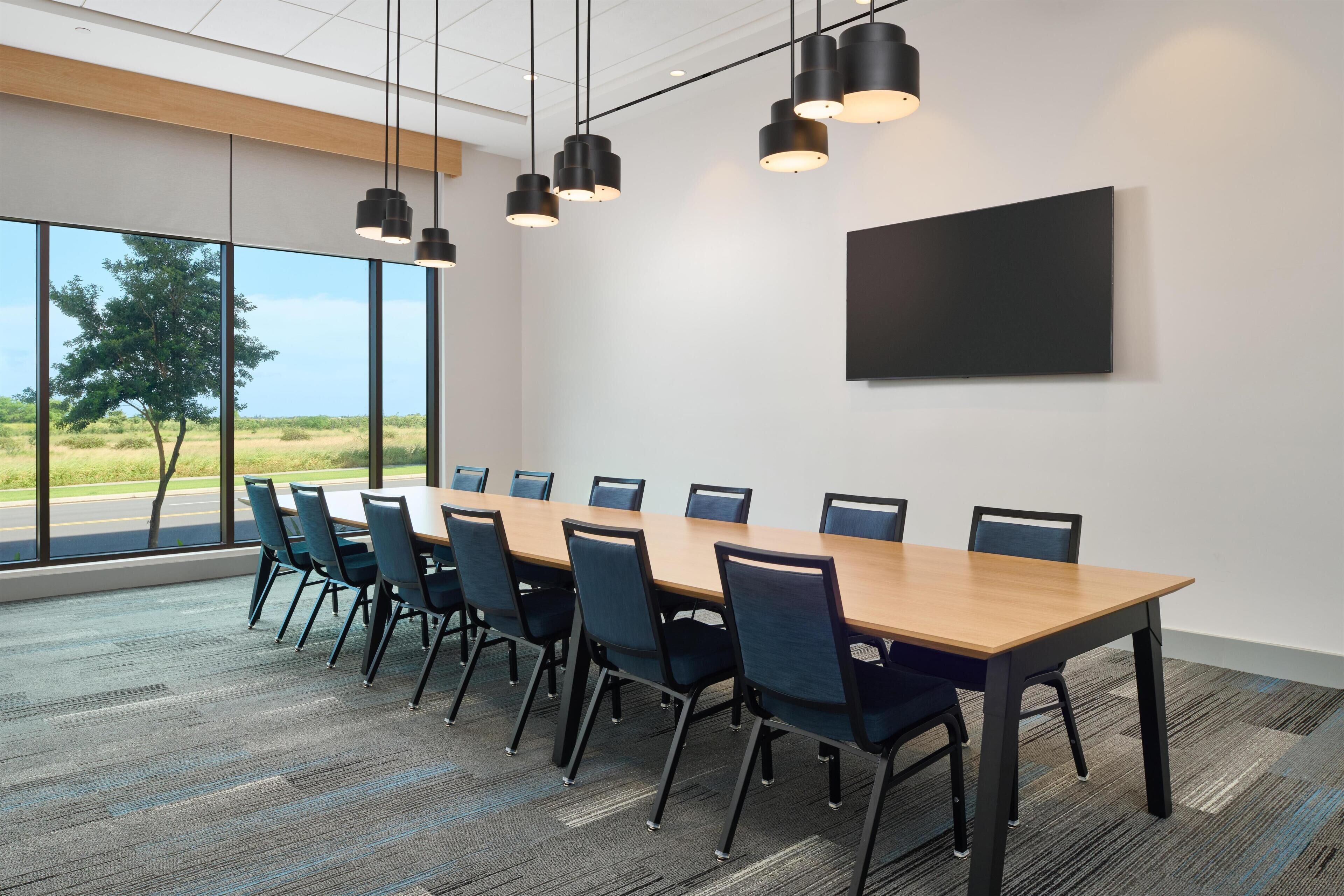 Een vergaderzaal met een lange tafel, stoelen en hangende verlichting.