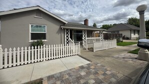 Uma casa residencial com varanda, cerca de piquete e entrada para carros.
