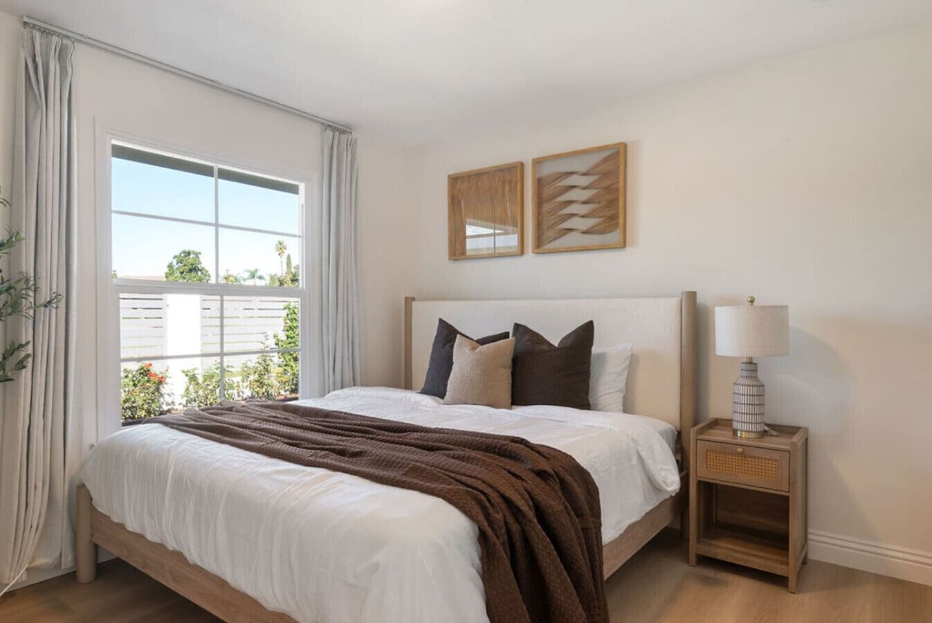 Un dormitorio ordenado con una cama grande, una lámpara de noche y una ventana con cortinas.