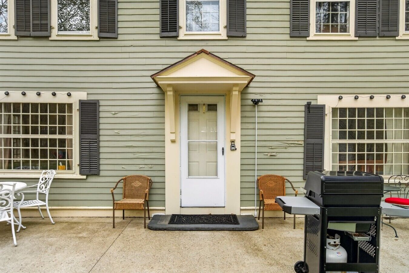 Une maison à deux étages avec un porche à l’avant, une porte blanche et deux fauteuils en osier.