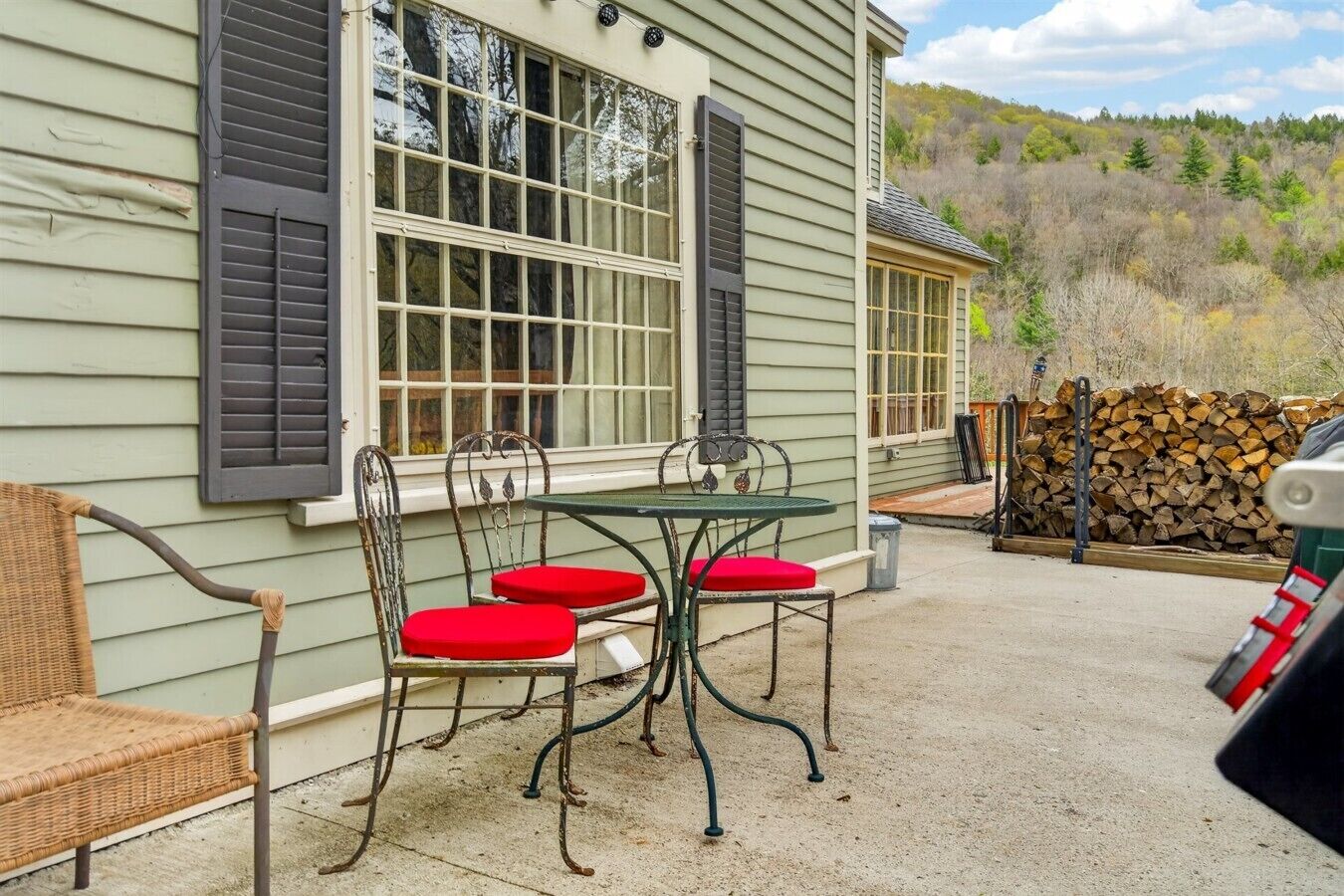 A patio with a table and chairs, a wicker chair, and a stack of firewood.