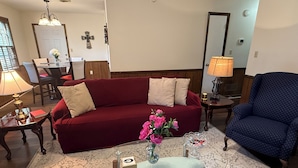 En stue med en rød sofa, en blå lænestol, et glasbord og en vase med blomster.