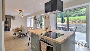 A modern kitchen with a central island, a built-in oven, and a large window overlooking a garden. - Le refuge du Mesnil - MESNIL-ROC'H (MESNIL-ROC'H)