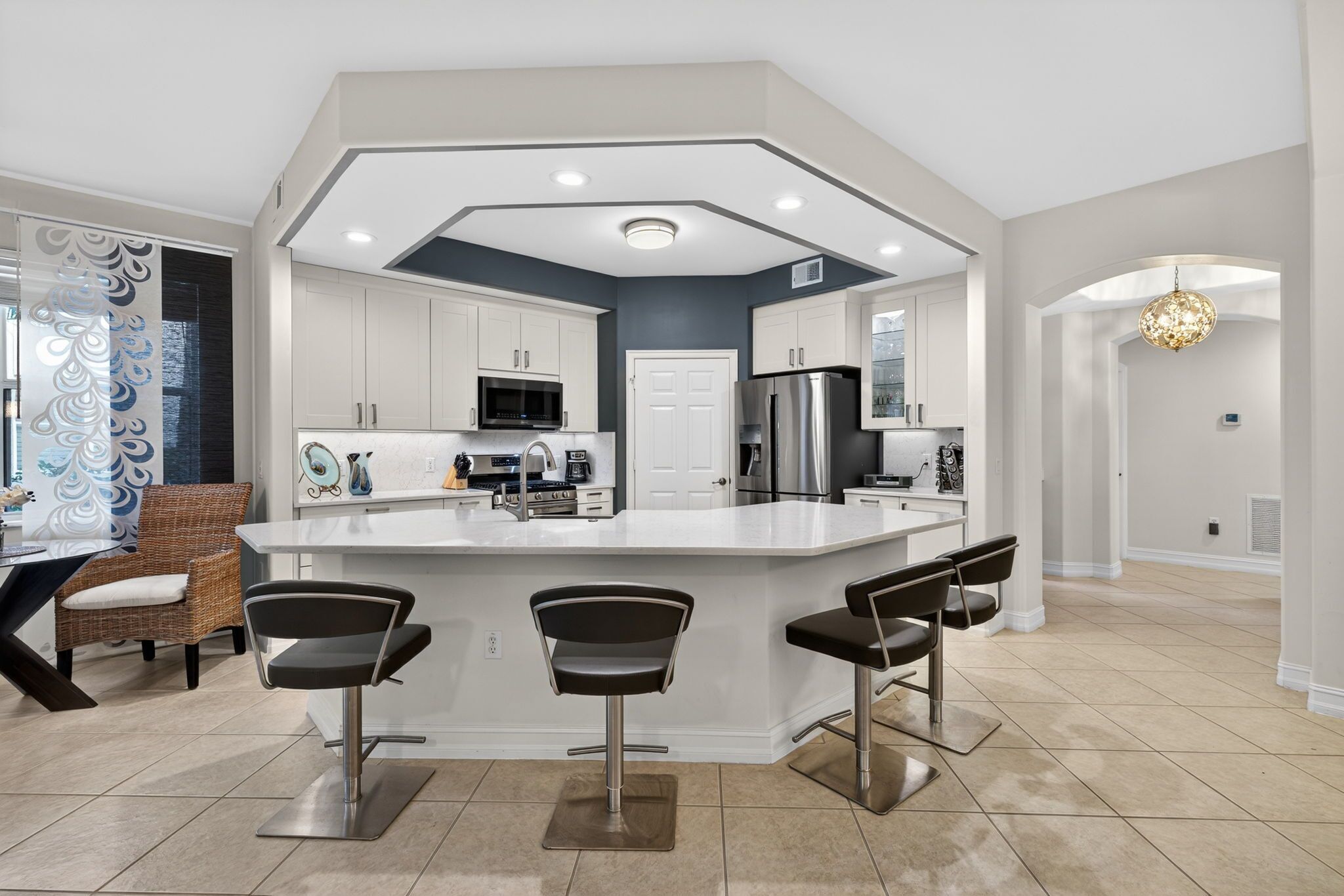A modern kitchen with a central island, bar stools, and a dining area with a wicker chair.