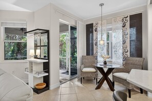 Ein modernes Wohnzimmer mit Glastür zum Balkon, einem Essbereich mit Korbstühlen und einem weißen Konsolentisch mit Lampe.