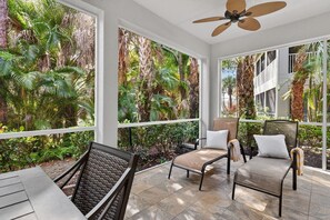 Eine sonnendurchflutete Terrasse mit Deckenventilator, zwei gepolsterten Stühlen und einem Korbstuhl.