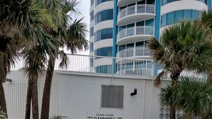 A gated entrance with a 'NO VANS or TRUCKS' sign, palm trees, and a modern building in the background. - Direct Oceanfront Balcony, 23rd Floor, Peck Plaza Building, Daytona Beach Shores (Daytona Beach Shores)