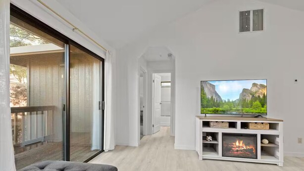 A modern living room with a flat-screen TV on a white entertainment unit, a fireplace, and a sliding glass door leading to an outdoor area. - Game Room, 8 guests- Lake, Yosemite, Sonora nearby (Groveland)