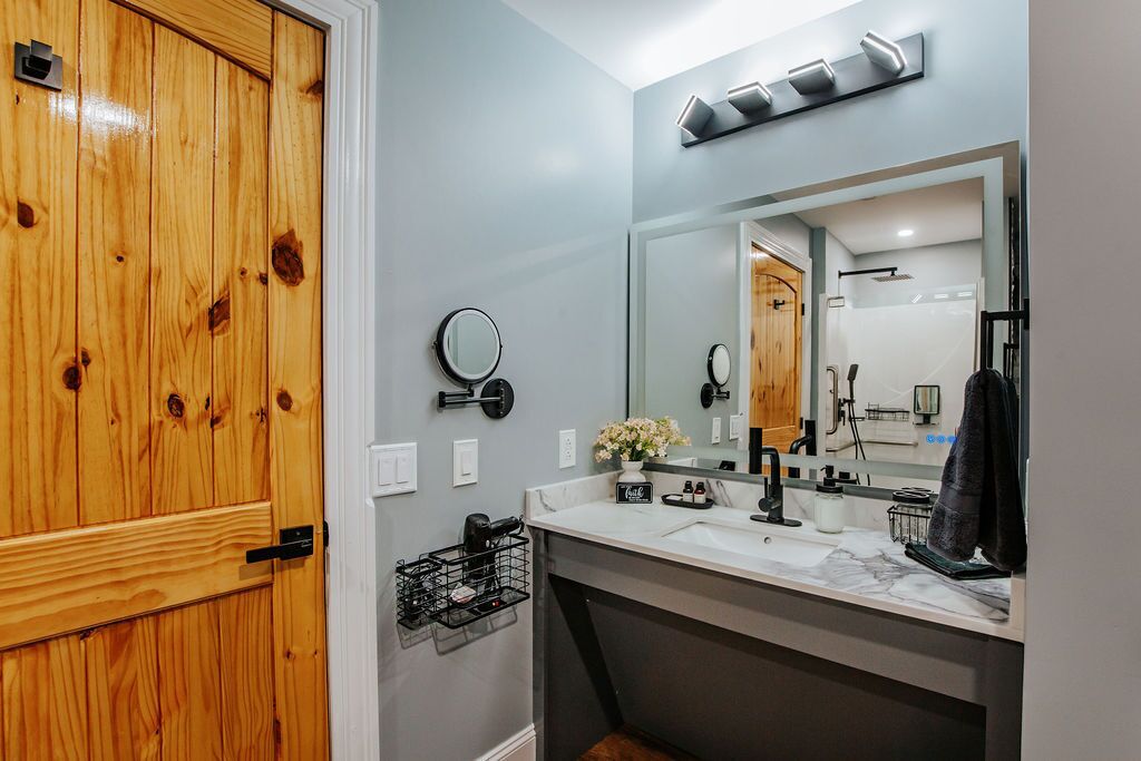 A bathroom with a wooden door, a large mirror, a sink, and a shower area.