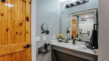 A bathroom with a wooden door, a large mirror, a sink, and a shower area.