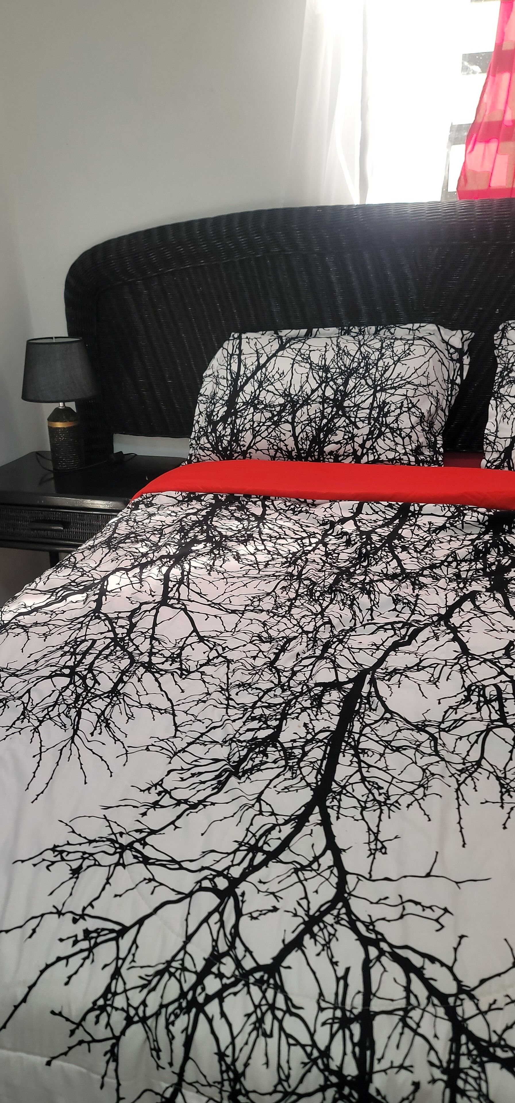 A bed with a black and white tree pattern bedspread and a red accent.