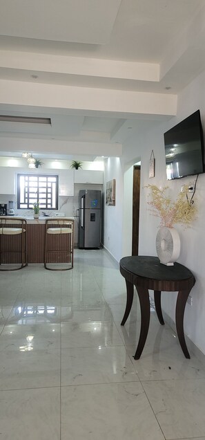 A modern kitchen with a refrigerator, a dining area with stools, and a flat-screen TV mounted on the wall. - LOVELY 3 BEDROOM APARTMENT OCEAN FRONT WITH POOL IN CALETA BEACH. (La Romana - Playa caleta)