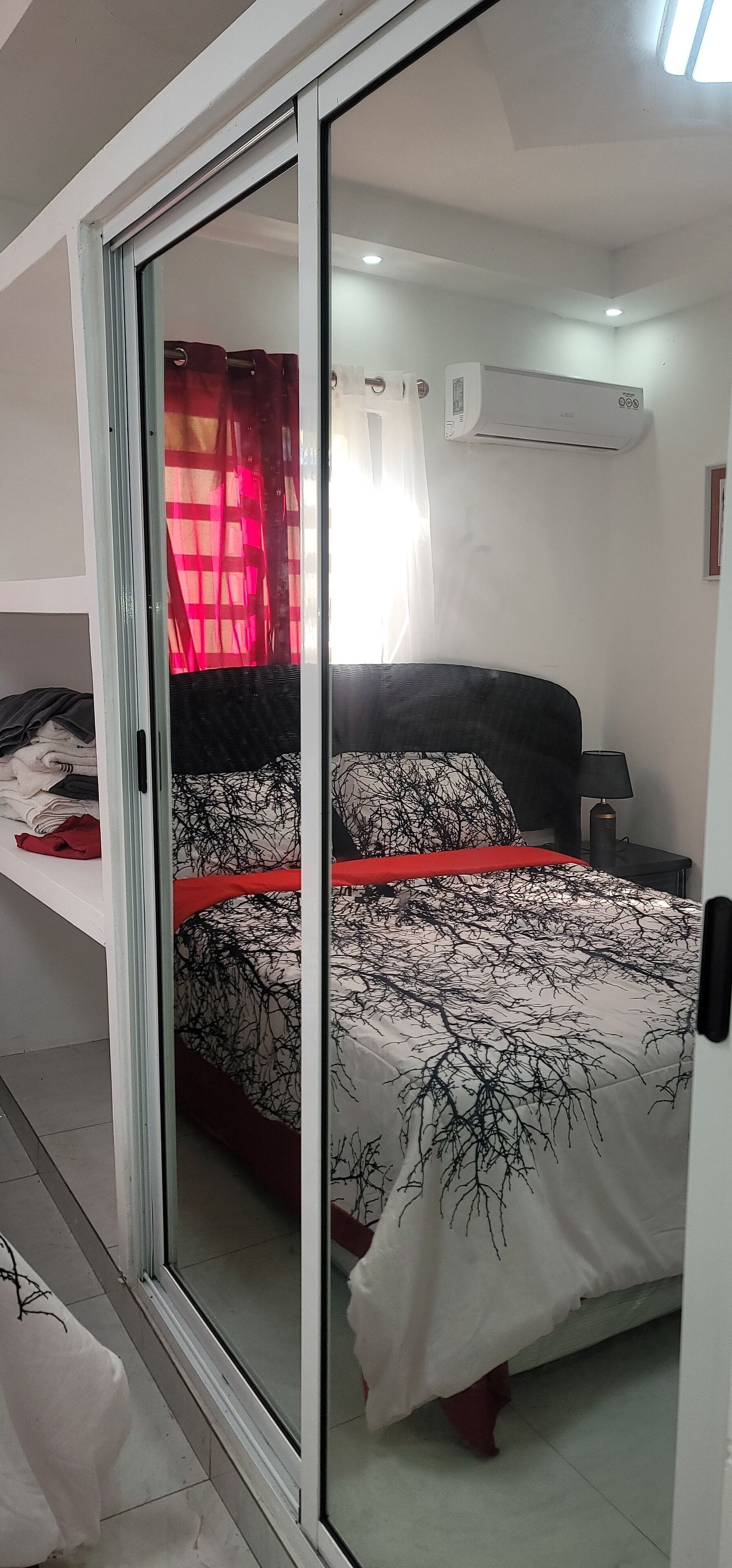 Une chambre à coucher avec un lit, une porte-fenêtre coulissante, un rideau rouge et un appareil de climatisation.