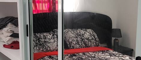 Une chambre à coucher avec un lit, une porte-fenêtre coulissante, un rideau rouge et un appareil de climatisation.