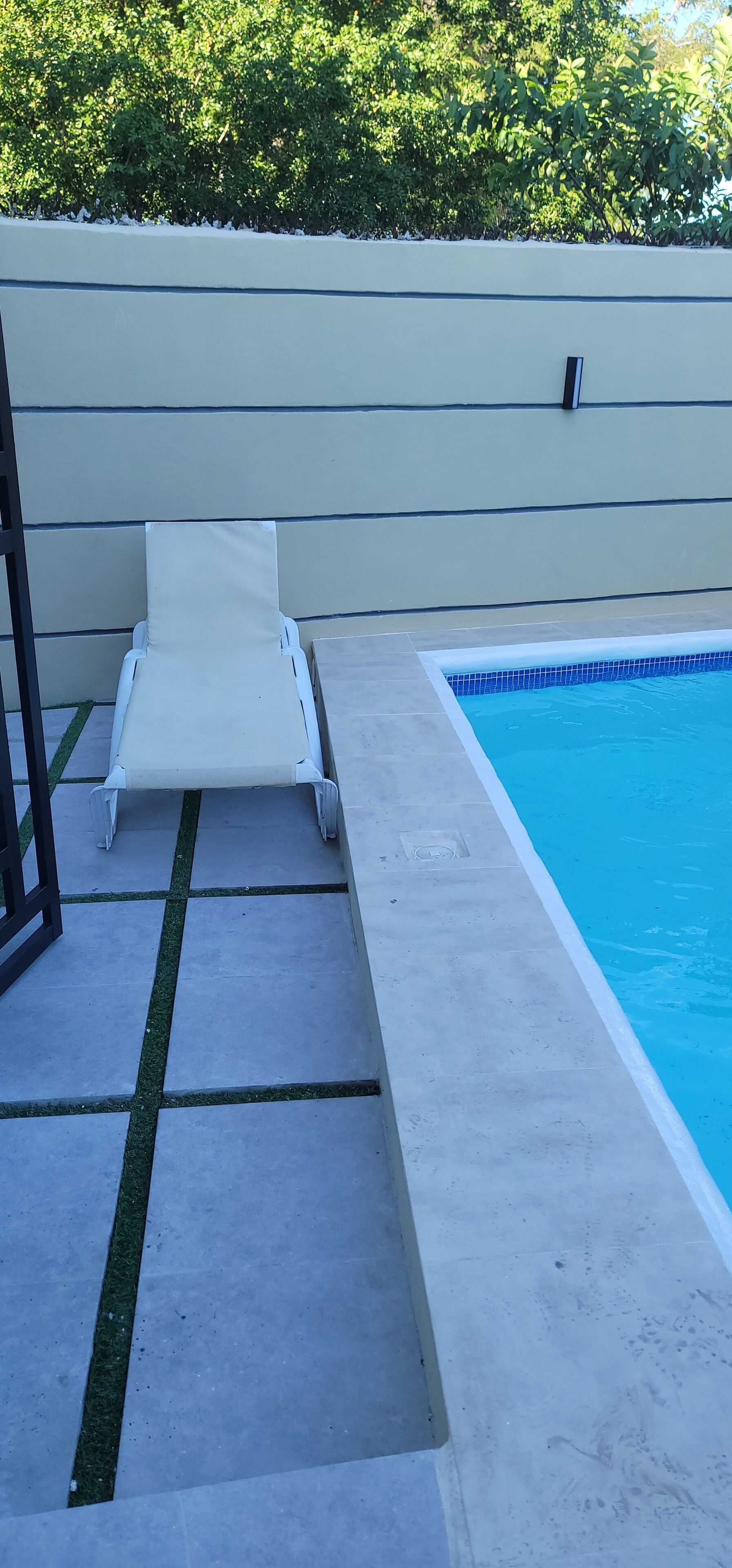 Ein Schwimmbecken mit einer weißen Liege und einer gefliesten Poolterrasse.