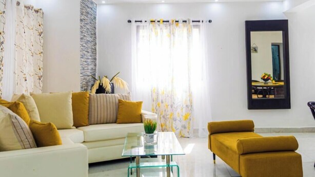 Uma sala de estar moderna com um sofá branco, uma mesa de centro de vidro e uma poltrona cor mostarda.