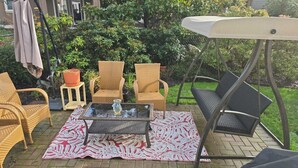 An outdoor patio with wicker chairs, a glass table, and a swing chair.