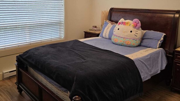 A bedroom with a wooden bed, a nightstand, a window with blinds, and a ceiling light.