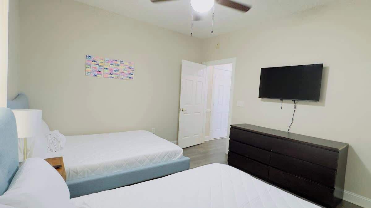 A bedroom with two beds, a dresser, a television, and a ceiling fan.