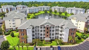 A multi-story residential building with a central courtyard, surrounded by parking and greenery. - Coastal Comfort 3BR Condo Balcony  Elevator (Myrtle Beach)