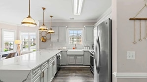 A modern kitchen with white cabinetry, a large island, stainless steel appliances, and pendant lighting. - Coastal Comfort 3BR Condo Balcony  Elevator (Myrtle Beach)