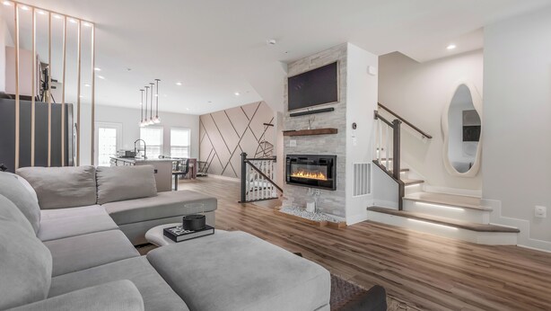 En moderne stue med en hjørnesofa, pejs og en trappe til en etage ovenover.
