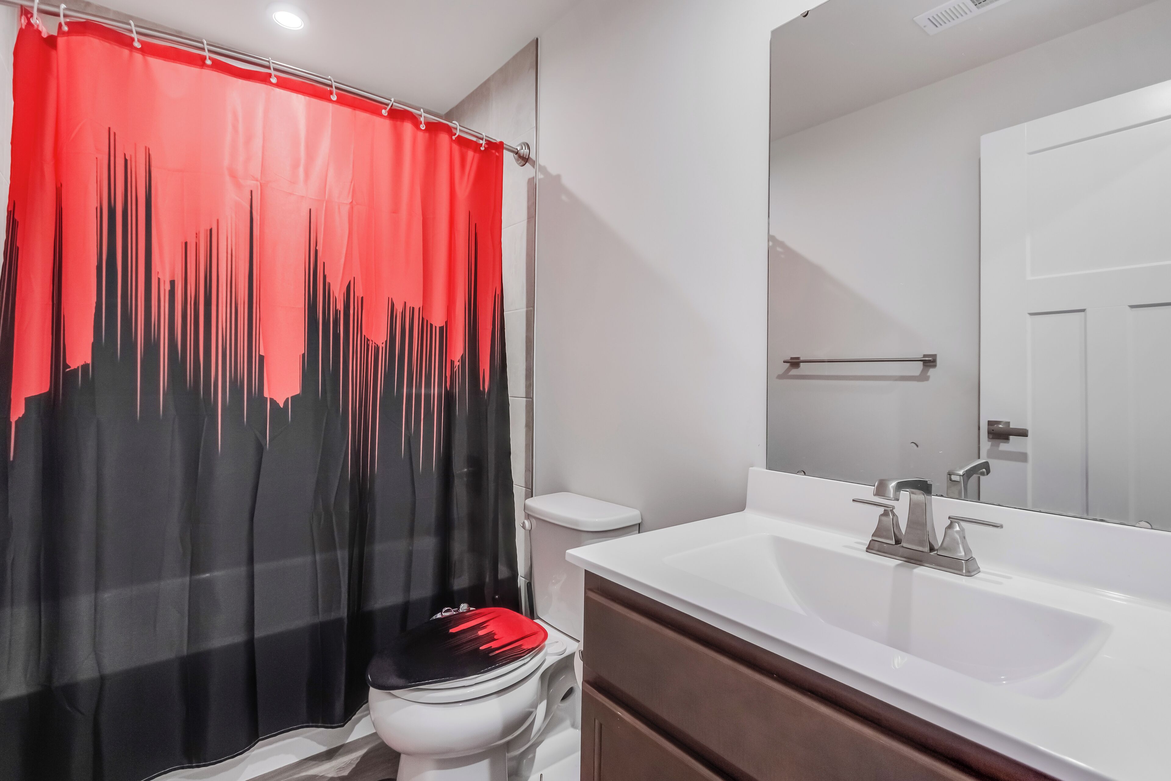 A modern bathroom with a white sink, a mirror, and a shower curtain with a red and black design.