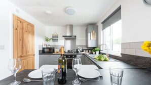 A modern kitchen with a central island, a wooden door, and a view of the outdoors. - Wheal Prosper, Wheal Dream - Hot Tub - Free Parking & WiFi - Pet Friendly (Helston)