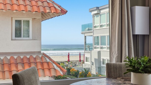 Una habitación con vista a la playa, un balcón con sombrillas rojas y una planta en maceta sobre la mesa.