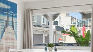 Un comedor moderno con una mesa, sillas, ventilador de techo y vistas a edificios a través de amplios ventanales.