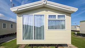 A small, single-story mobile home with a pitched roof, large windows, and a satellite dish. - Brand New Luxury Silver Caravan (Ingoldmells, Skegness)