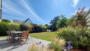 Eine Terrasse mit Tisch und Stühlen, umgeben von einem Garten mit verschiedenen Pflanzen und Blumen.