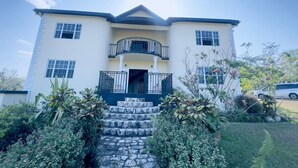 A two-story house with a balcony, a front door, and a staircase leading to the entrance. - Fabulous 4-bedroom house with AC in charming Bog Walk (Bog Walk)