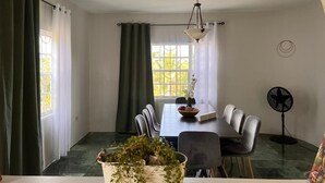 A dining area with a table, chairs, a fan, and a window with curtains. - Fabulous 4-bedroom house with AC in charming Bog Walk (Bog Walk)