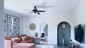 Een moderne woonkamer met een roze bank, een plafondventilator, een televisie en een decoratief wandobject.