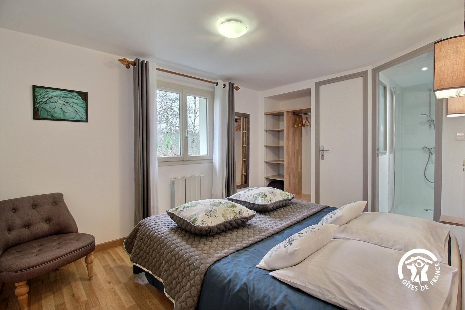 Ein Schlafzimmer mit Bett, Sessel, Kleiderschrank und Fenster.
