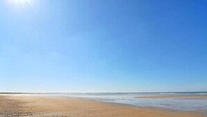 Une vaste plage, avec un ciel dégagé et une mer calme.