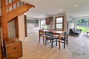 A modern kitchen with white cabinets, a dining area with a wooden table and chairs, a sofa, and a staircase. - Ti Bihan - MOREAC - Gîte (MOREAC)