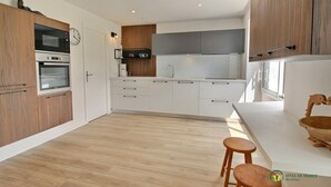 Una cucina moderna con mobili bianchi, forno integrato, microonde e macchina per il caffè. È presente un tavolo da pranzo in legno con due sgabelli.
