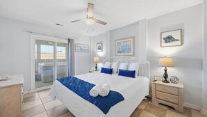 A hotel room with a bed, a nightstand, a ceiling fan, a sliding glass door, and a view of the beach. - Wink Shores | Oceanfront | Private Pool, Hot Tub, and Dog Friendly (Kill Devil Hills)